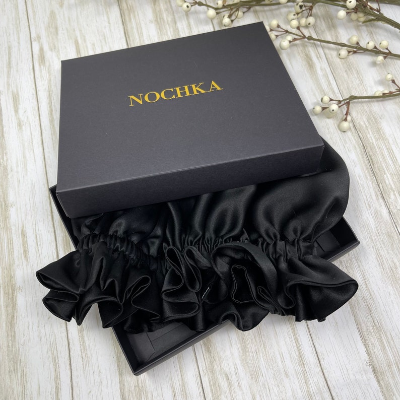 May include: A black satin hair bonnet with ruffles, packaged in a black box with the word "NOCHKA" printed in gold lettering.