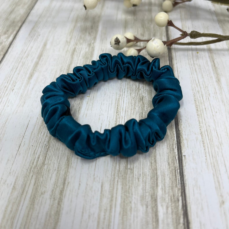 K&ouml;nnte beinhalten: Ein blauer Satin-Haargummi in Teal. Der Haargummi ist aus weichem, seidenweichem Stoff gefertigt und wurde entwickelt, um schonend zu den Haaren zu sein.