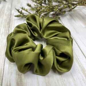 May include: A green satin scrunchie hair tie. The scrunchie is made of soft, silky fabric and is designed to be gentle on hair.