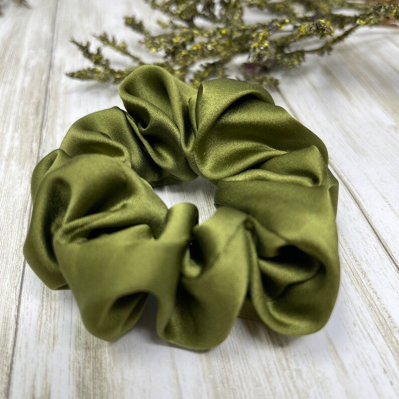 May include: A green satin scrunchie hair tie. The scrunchie is made of soft, silky fabric and is designed to be gentle on hair.