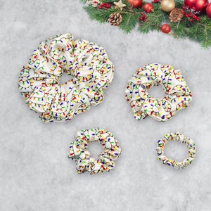 May include: Three white satin scrunchies with a colorful Christmas lights pattern. The scrunchies are different sizes.