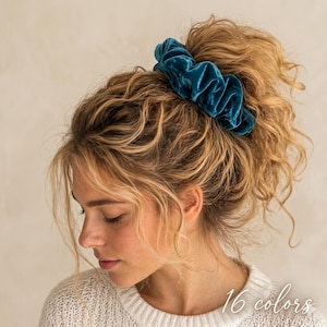 May include: A teal velvet scrunchie worn in a high bun. The scrunchie is a deep shade of teal and appears soft and plush. The image also includes the text "16 colors" in a script font.