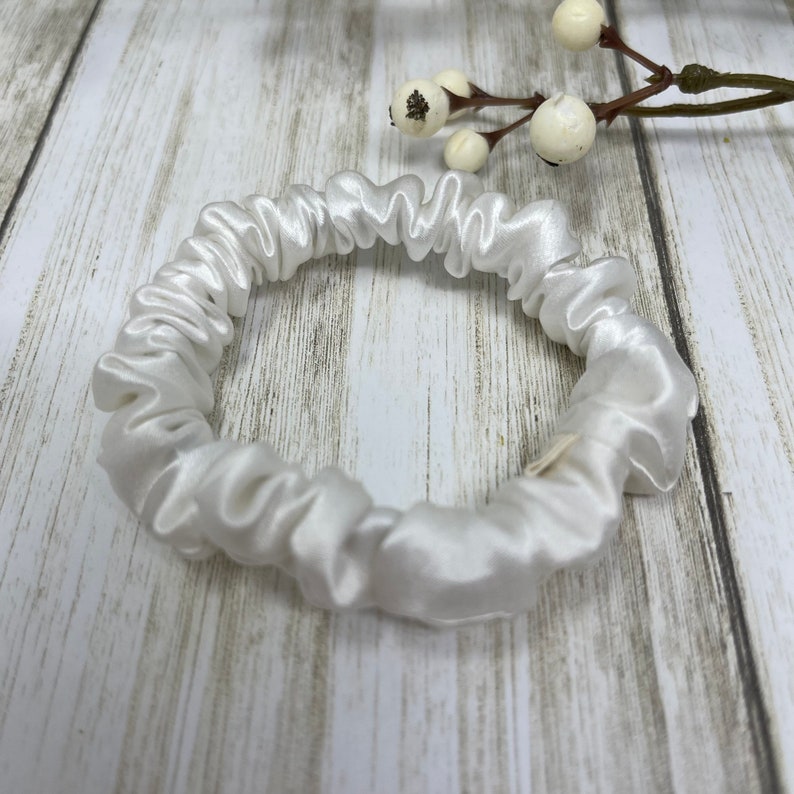 K&ouml;nnte beinhalten: Ein wei&szlig;er Satin-Haargummi. Der Haargummi ist aus weichem, glattem Stoff gefertigt und wurde entwickelt, um schonend zu den Haaren zu sein.