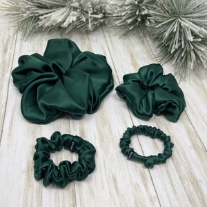May include: Four green satin scrunchies of different sizes. The largest scrunchie is in a gathered, bunched style. The other three scrunchies are in a simple, circular style.