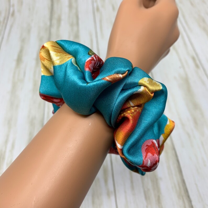 May include: Teal blue satin scrunchie with a floral print featuring yellow, orange, and red flowers.