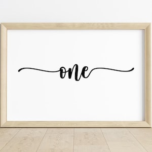 Pode incluir: Impressão emoldurada com a palavra "one" em elegante escrita preta. A palavra está centrada em um fundo branco, com uma linha fluida acima e abaixo. A moldura é de madeira clara, e a impressão está em um chão de madeira.