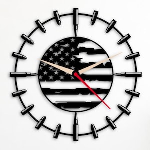 Könnte beinhalten: Eine schwarze Metall-Wanduhr mit einem Design der amerikanischen Flagge. Das Zifferblatt der Uhr ist die Flagge, umgeben von schwarzen Patronenhülsen. Die Zeiger der Uhr sind beige, mit einem roten Sekundenzeiger.