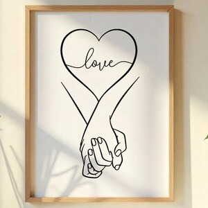 Puede incluir: Una impresión enmarcada con un dibujo lineal negro de dos manos entrelazadas, formando un corazón. La palabra "love" está escrita dentro del corazón. El marco es de color marrón claro.