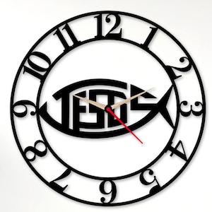 May include: Black wall clock with the word "JESUS" inside a fish symbol. The clock has a black circular frame with numbers and hands. The second hand is red. The clock is on a white wall.