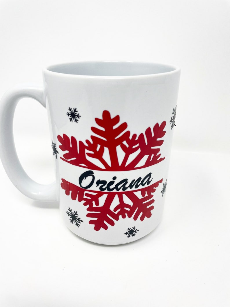 May include: White ceramic mug with a red snowflake design and the name "Oriana" written in black.