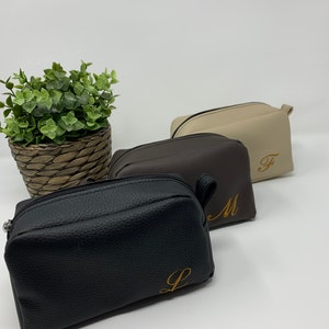 May include: Three zippered pouches in black, brown, and beige with gold embroidered initials "L", "M", and "F".