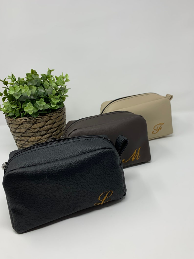 May include: Three zippered pouches in black, brown, and beige with gold embroidered initials "L", "M", and "F".