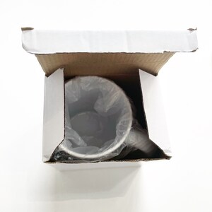 May include: A white cardboard box with the top open, revealing a silver stainless steel travel mug inside. The mug is wrapped in clear plastic.