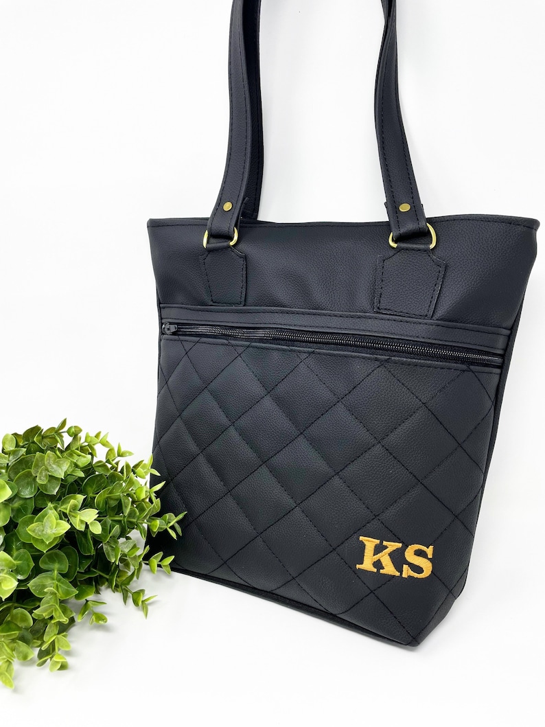 May include: Black quilted tote bag with gold hardware and a zippered pocket. The bag has the initials "KS" embroidered on the front in gold thread.