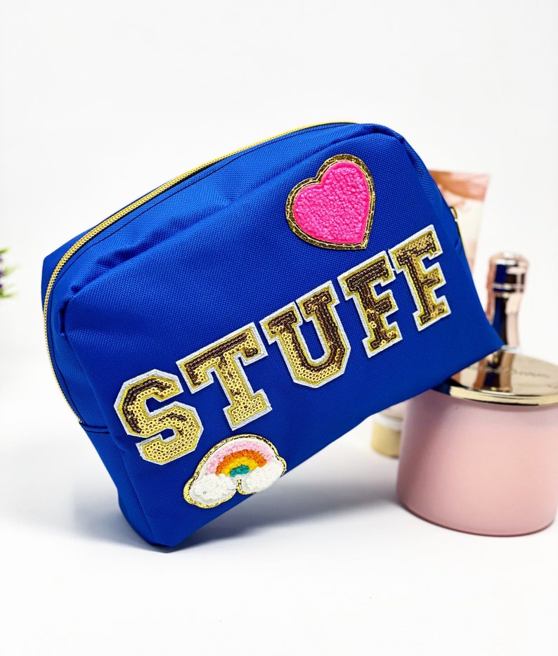 Op de afbeelding: Een felblauwe ritszak met een gouden glitter "STUFF" patch, een roze hart patch en een regenboog patch.
