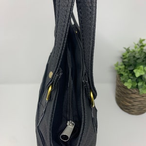 May include: A black leather tote bag with gold hardware and a zipper closure. The bag has two top handles and a zippered pocket on the front.