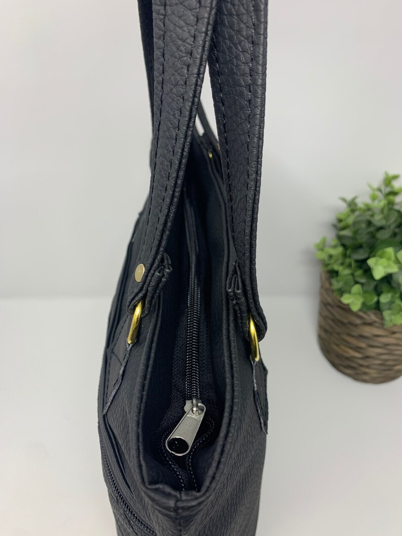 May include: A black leather tote bag with gold hardware and a zipper closure. The bag has two top handles and a zippered pocket on the front.
