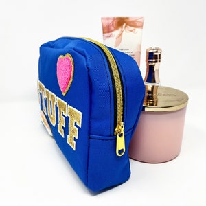 Op de afbeelding: Een blauwe toilettas met een gouden rits en een gouden geborduurde patch met de tekst "STUFF" en een roze hartpatch.