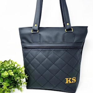 May include: Black quilted tote bag with gold hardware and a zippered pocket. The bag has the initials "KS" embroidered on the front in gold thread.