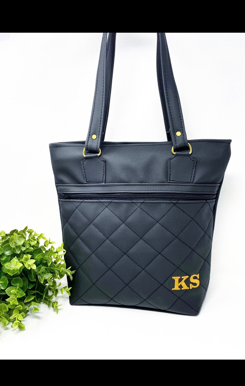 May include: Black quilted tote bag with gold hardware and a zippered pocket. The bag has the initials "KS" embroidered on the front in gold thread.