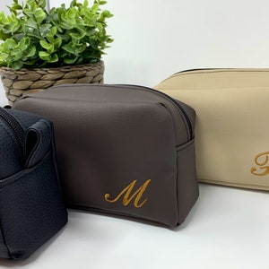 May include: Three zippered toiletry bags with personalized embroidered initials. The bags are in black, brown, and beige.