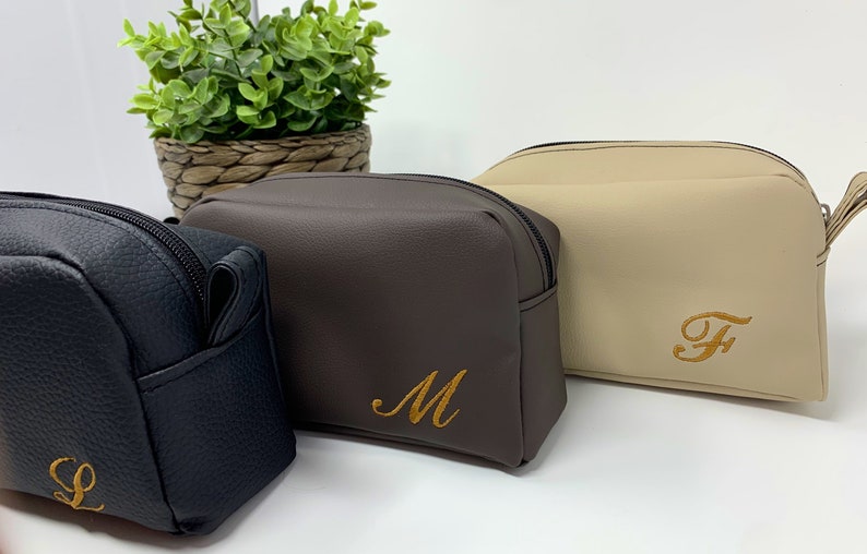 May include: Three zippered toiletry bags with personalized embroidered initials. The bags are in black, brown, and beige.