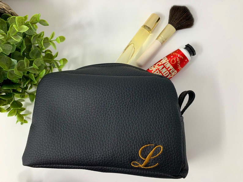 May include: Black leather zippered makeup bag with a gold embroidered letter L.