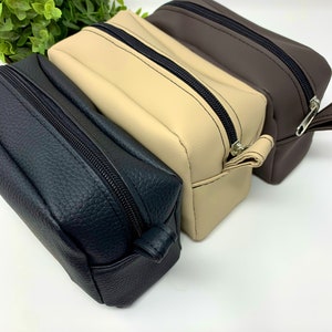 May include: Three zippered pouches in black, beige, and brown leather. The pouches are stacked on top of each other.