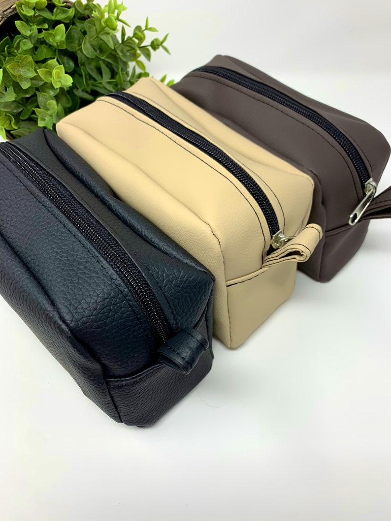 May include: Three zippered pouches in black, beige, and brown leather. The pouches are stacked on top of each other.