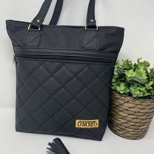 May include: Black quilted tote bag with gold hardware and a zippered pocket. The bag has a gold label with the text "OMMO" on it. A black tassel keychain with a gold clasp is included.