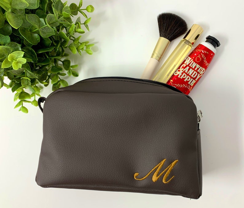 May include: A brown faux leather zippered travel makeup bag with a gold embroidered letter M.