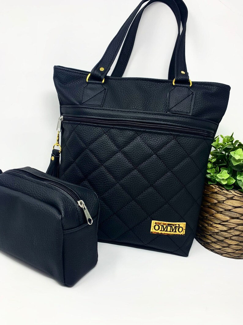 May include: Black quilted tote bag with gold hardware and a matching black zippered pouch. The tote bag has a gold label with the text "OMMO" on it.