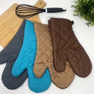 May include: Three quilted oven mitts in gray, teal, and brown. The mitts are made of a soft, quilted fabric and have a loop for hanging.