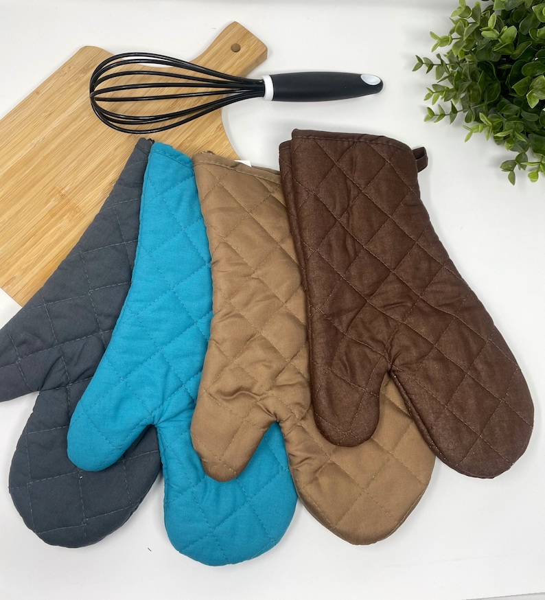 May include: Three quilted oven mitts in gray, teal, and brown. The mitts are made of a soft, quilted fabric and have a loop for hanging.