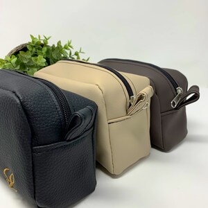 May include: Three zippered pouches in black, beige, and brown. The pouches are made of a textured faux leather material.