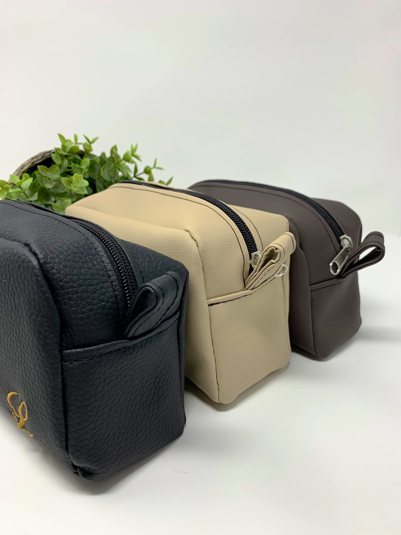 May include: Three zippered pouches in black, beige, and brown. The pouches are made of a textured faux leather material.