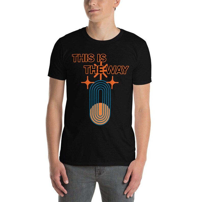 K&ouml;nnte beinhalten: Schwarzes T-Shirt mit dem Text "This is the way" in orangefarbener und schwarzer Schrift. Unter dem Text befindet sich ein stilisiertes orangefarbenes und blaues Symbol.