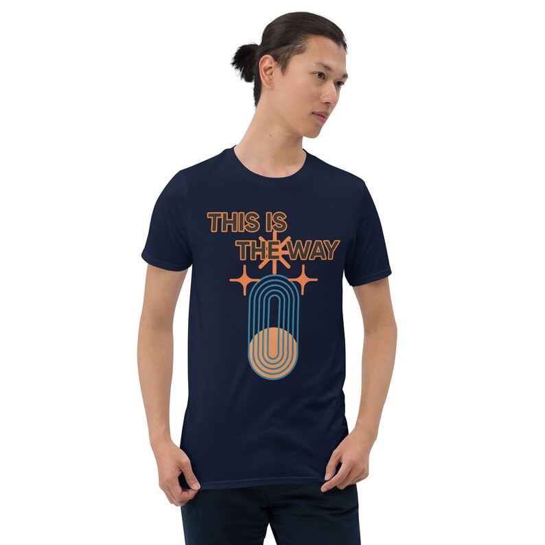 K&ouml;nnte beinhalten: Ein marineblaues T-Shirt mit einem Grafikdesign im Retro-Stil. Die Grafik zeigt eine stilisierte Sonne mit Strahlen, einen Kreis mit konzentrischen Linien und den Text "This is the way".