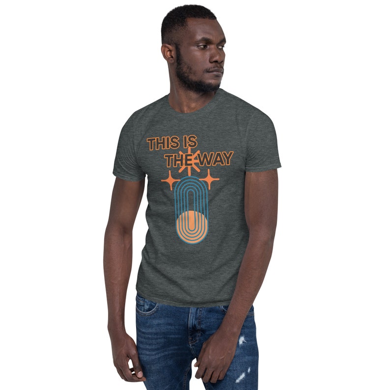 K&ouml;nnte beinhalten: Ein dunkel-melierter grauer T-Shirt mit einem Grafikdesign im Retro-Stil. Die Grafik zeigt eine stilisierte Sonne mit Strahlen und den Text "This is the Way".