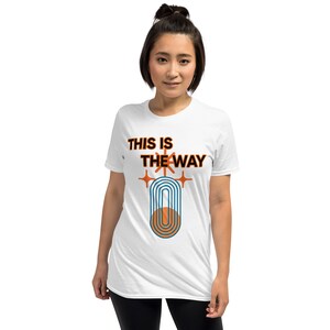 K&ouml;nnte beinhalten: Wei&szlig;es T-Shirt mit dem Text "This is the way" in Schwarz, einer stilisierten Grafik in Orange und Blau und zwei orangefarbenen Sternen.