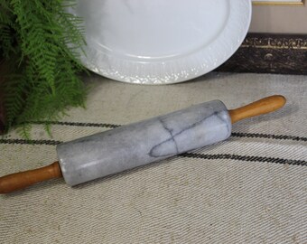May include: A gray marble rolling pin with wooden handles. The rolling pin is lying on a white and black striped fabric.
