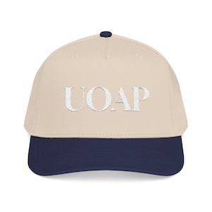 May include: A baseball cap with a beige crown and a navy blue brim. The cap features the embroidered letters "UOAP" in a silver, textured font across the front. The top button is navy blue.