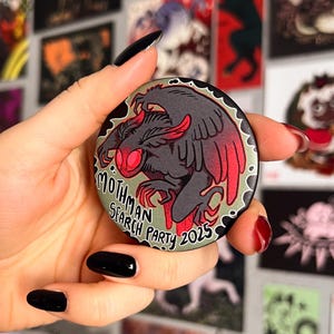 以下が含まれることがあります： 黒と赤のモスマンのイラストが描かれた丸いボタン。モスマンの周りに白い円の中に「モスマンサーチパーティー2025」という文字が書かれている。