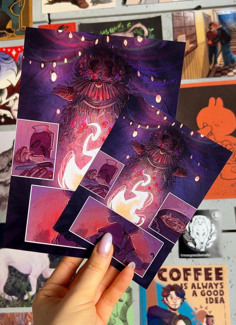 May include: Two illustrated prints featuring a whimsical character with a crown of flowers and glowing lights. The character is surrounded by a purple and pink background with a fire and a cup of coffee in the foreground. The text "Coffee is always a good idea" is visible in the bottom right corner.