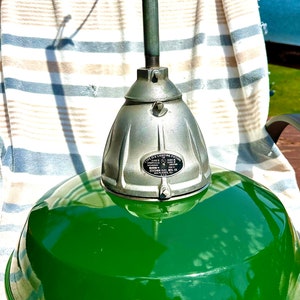 May include: A green metal industrial pendant light fixture with a silver metal canopy. The fixture has a label that reads "Type 'HG' Lighting Fixture, Class 'B' Insulation, Hazardous Location, 1000 Watts, 125 Volts, 8 Amps, Brown Electric Mfg. Co., Des Plaines, Ill., U.S.A."