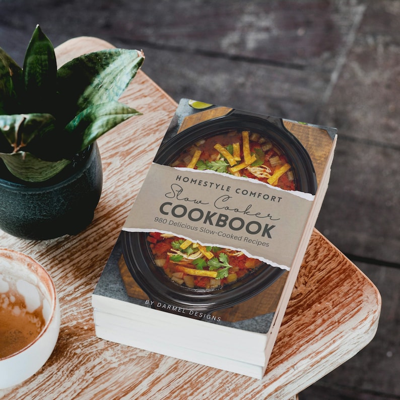 May include: A cookbook titled "Homestyle Comfort Slow Cooker Cookbook" with a photo of a slow cooker filled with a stew on the cover. The text on the cover reads "980 Delicious Slow-Cooked Recipes" and "By Darmel Designs".