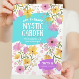 Pode incluir: Uma capa de livro com um design de aquarela de flores rosa e amarelas sobre um fundo branco. O título é "Art Therapy Mystic Garden" com o subtítulo "28 desenhos florais e mandalas intrincados". A parte inferior da capa diz "Criado por Darmel Designs".