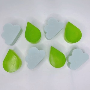 Puede incluir: Ocho jabones hechos a mano en forma de nubes y gotas de lluvia. Los jabones en forma de nube son de color azul claro y los jabones en forma de gota de lluvia son de color verde claro.
