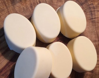 May include: Six round, white, oval-shaped soap bars on a wooden surface.