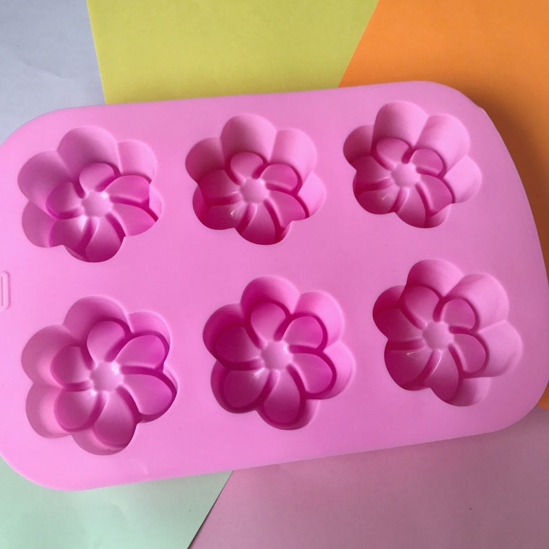 May include: Pink silicone mould with six flower-shaped cavities. The mould is designed for making small cakes, chocolates, or other treats.